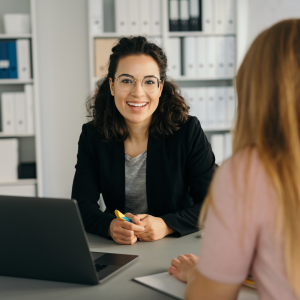 Woman sitting in front of a computer speaking to another person.