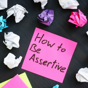 post-it how to be assertive with old crumpled up notes scattered in the background.